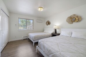 Un dormitorio con dos camas, una ventana con persianas, un equipo de aire acondicionado y decoración en la pared.