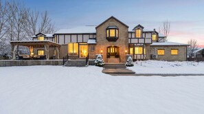 A large, multi-story house with a prominent entrance, a covered porch, and a snow-covered driveway.