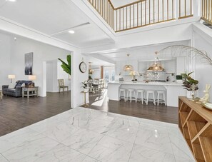 A spacious living area with a high ceiling, a dining area, and a kitchen with a bar.
