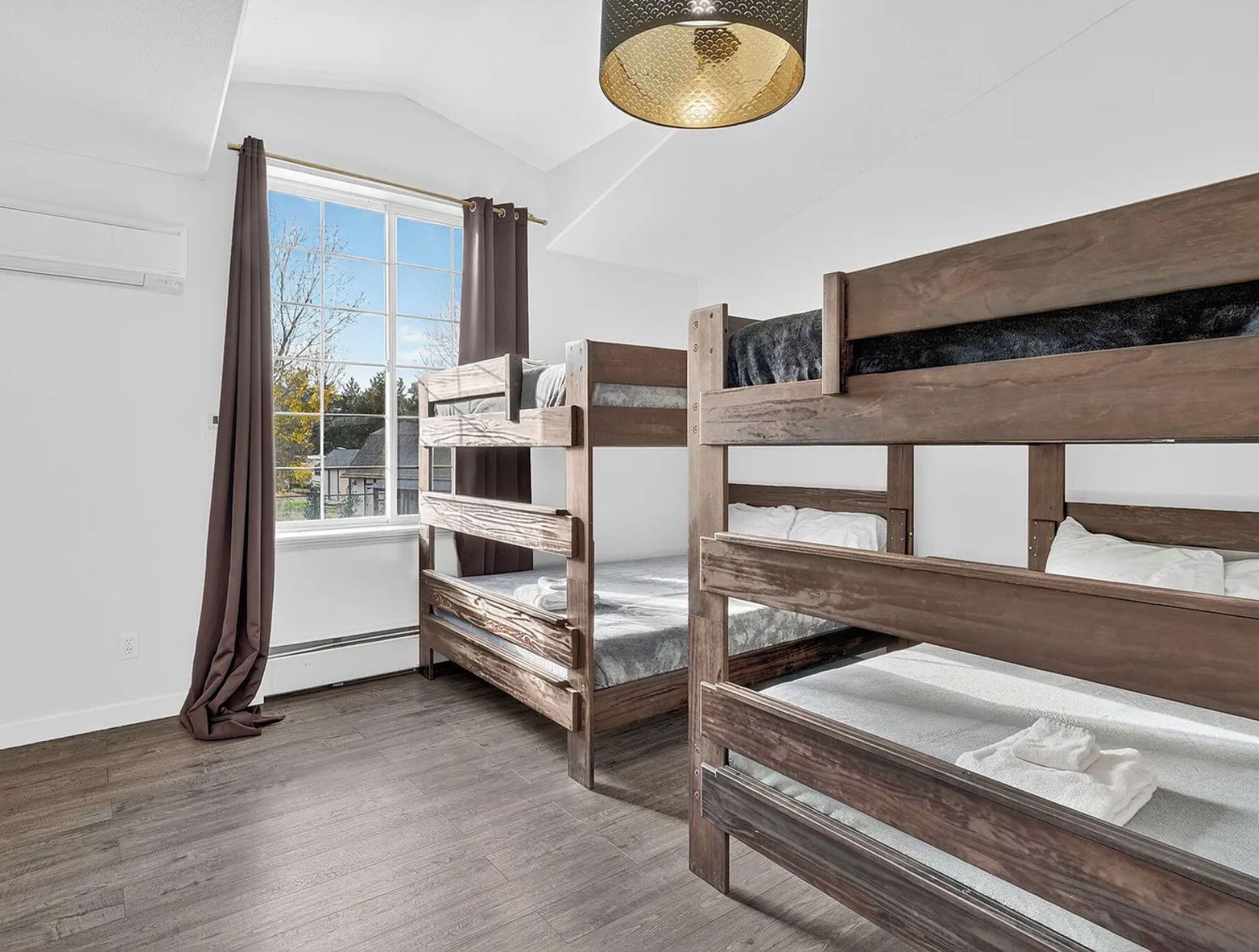 A room with bunk beds, a window with curtains, and a hanging light fixture.