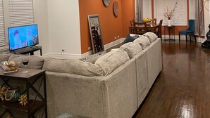 Un salon moderne avec un canapé d’angle, un coin repas comprenant une table et des chaises, et un téléviseur posé sur un meuble.