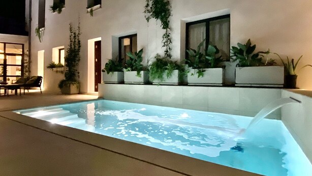 An indoor swimming pool with a clear water surface, surrounded by potted plants and a seating area with chairs. - Alaró Natura Rural Suites (Alaro)