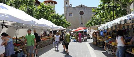 A market street with vendors and stalls, a church in the background, and pedestrians.