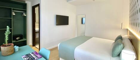 A modern hotel room with a bed, a desk, a chair, a TV, and a wardrobe.