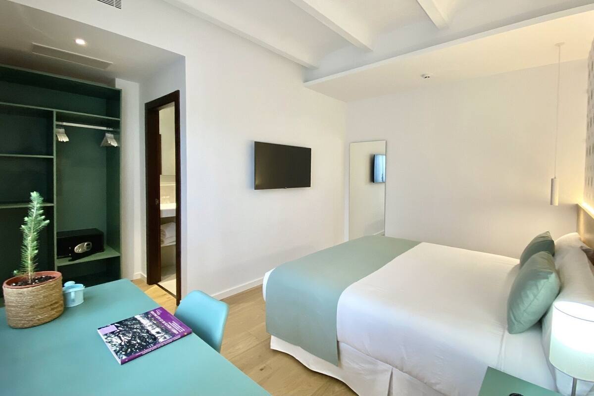 Quarto de hotel moderno com cama, escrivaninha, cadeira, televisão e guarda-roupa.