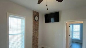 Habitació amb ventilador de sostre, rellotge, televisió de pantalla plana i finestra gran.