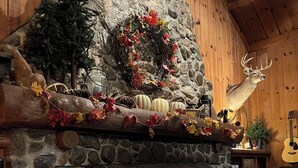 A cozy fireplace area with a stone mantle, a log fire, and a deer head decoration.