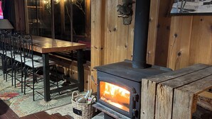 A cozy cabin interior with a wood-burning stove, a dining table, chairs, and a fireplace.
