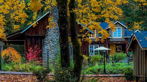 A rustic lodge with stone walls and wooden structures, surrounded by autumn foliage and a stone pathway.