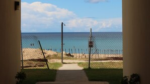 An arched pathway leading to a beach with a clear sky and a fence. - Beach Front (Rincón)