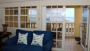 A room with a blue sofa, two decorative pillows, and a view of the beach through a sliding glass door. - Beach Front (Rincón)