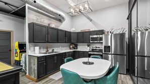 A modern kitchen with dark cabinets, stainless steel appliances, and teal chairs around a white table.