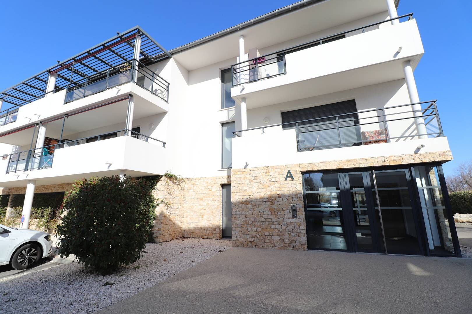 A modern multi-story building with balconies, a stone facade, and a clear sky.