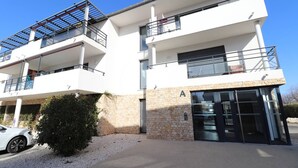 Un immeuble moderne à plusieurs étages, doté de balcons, d’une façade en pierre et surplombant un ciel dégagé.