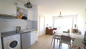 Une cuisine compacte équipée d’un lave-linge, un coin repas avec une table et des chaises, et un espace de vie comprenant un canapé et un téléviseur.