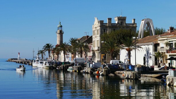 Une promenade en bord de mer avec des bateaux amarrés, un phare et des bâtiments historiques.