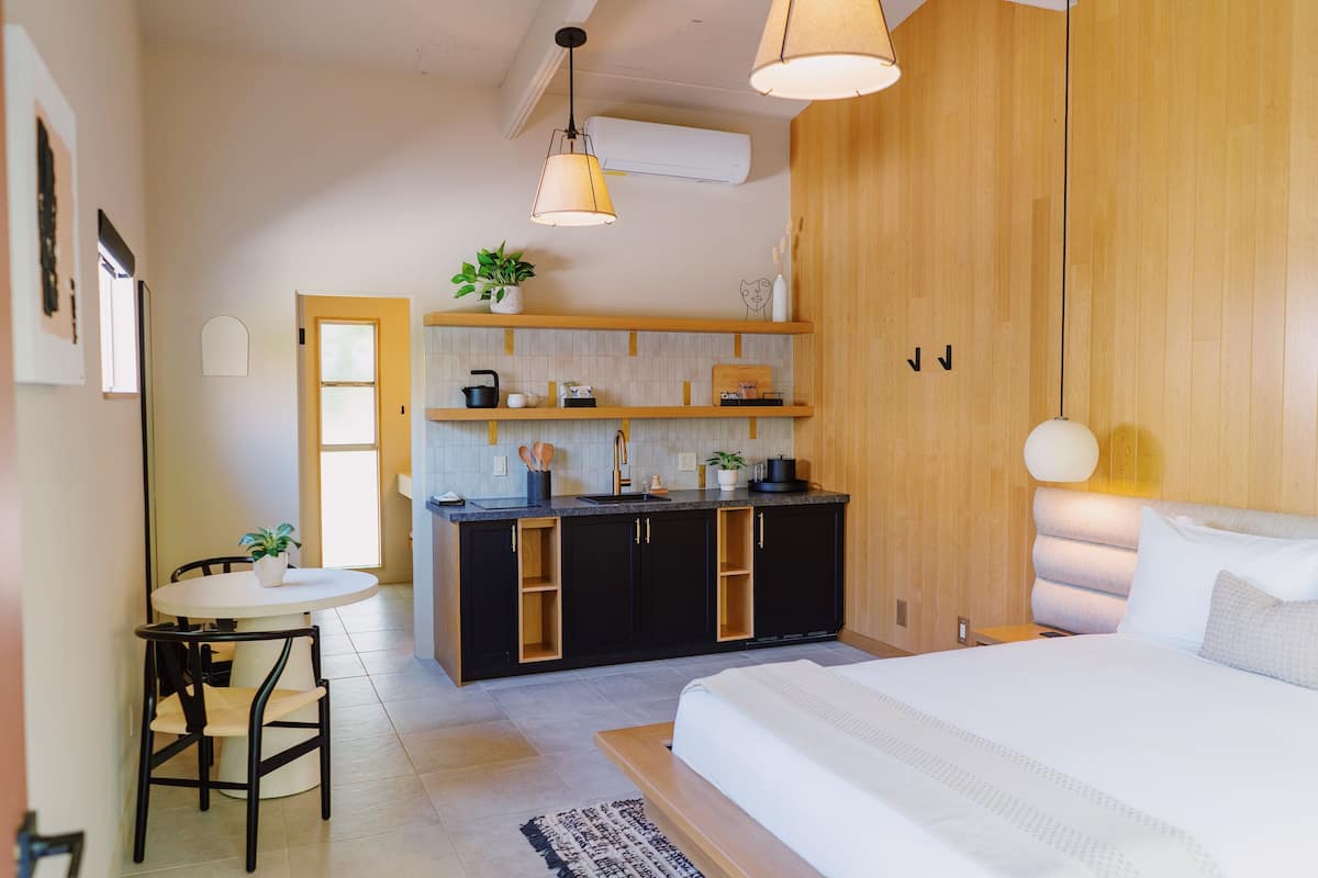 Una habitación de hotel moderna con una cama, una pequeña mesa de comedor, una zona de cocina y una pared decorativa de madera.