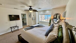 A bedroom with a bed, a ceiling fan, a TV, a window, and a mirror. - Epic Views, Huge House, Acres of J-Trees to explore + Hot Tub, Pool, AC & Golf! (Joshua Tree)
