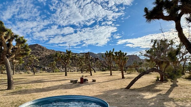 A hot tub in a desert landscape with trees and a mountain in the background. - Epic Views, Huge House, Acres of J-Trees to explore + Hot Tub, Pool, AC & Golf! (Joshua Tree)