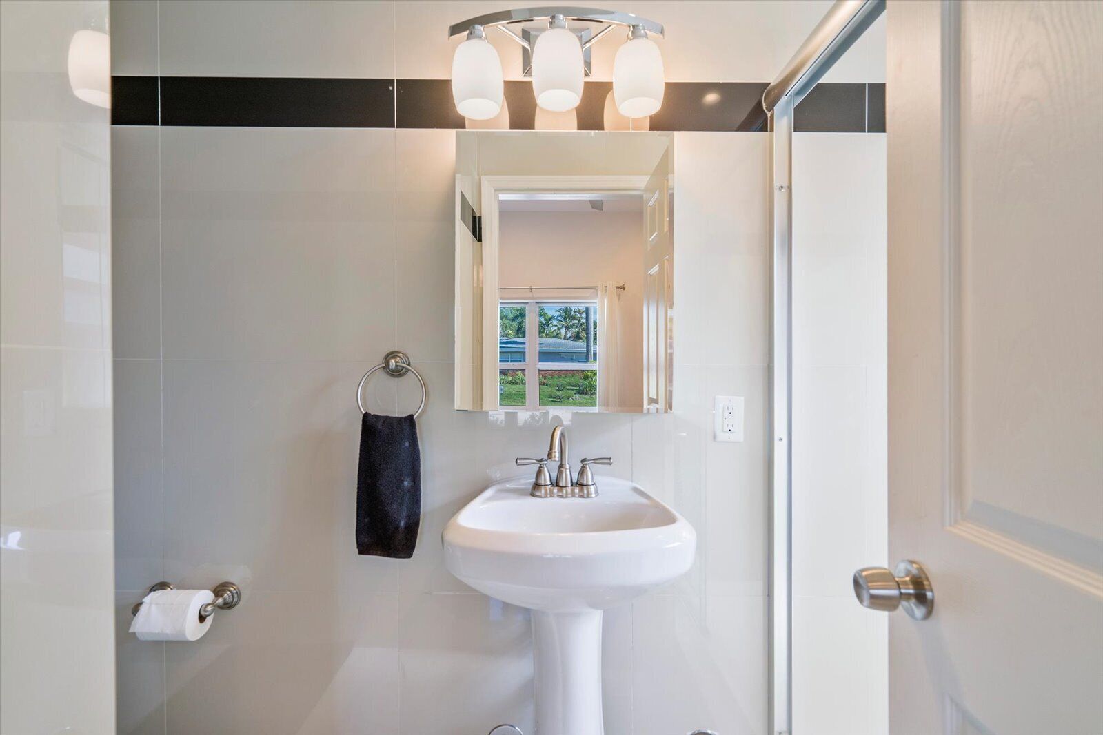 A bathroom with a white sink, a towel rack with a towel, a toilet paper holder, and a window with a view of greenery.