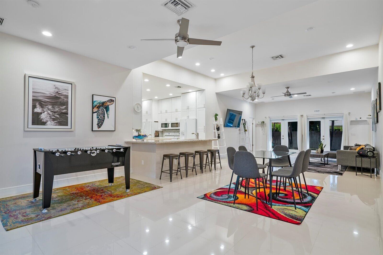 A spacious living area with a foosball table, a dining table with chairs, a chandelier, and a ceiling fan.