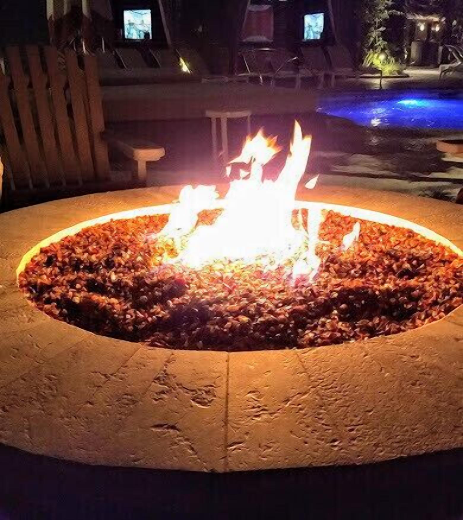 Un hogar circular al aire libre con un borde de piedra texturizada, rodeado por una terraza de madera.