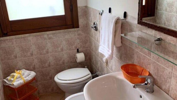 Een badkamer met toilet, bidet en wastafel. Handdoekrek en glazen plank met mandje.