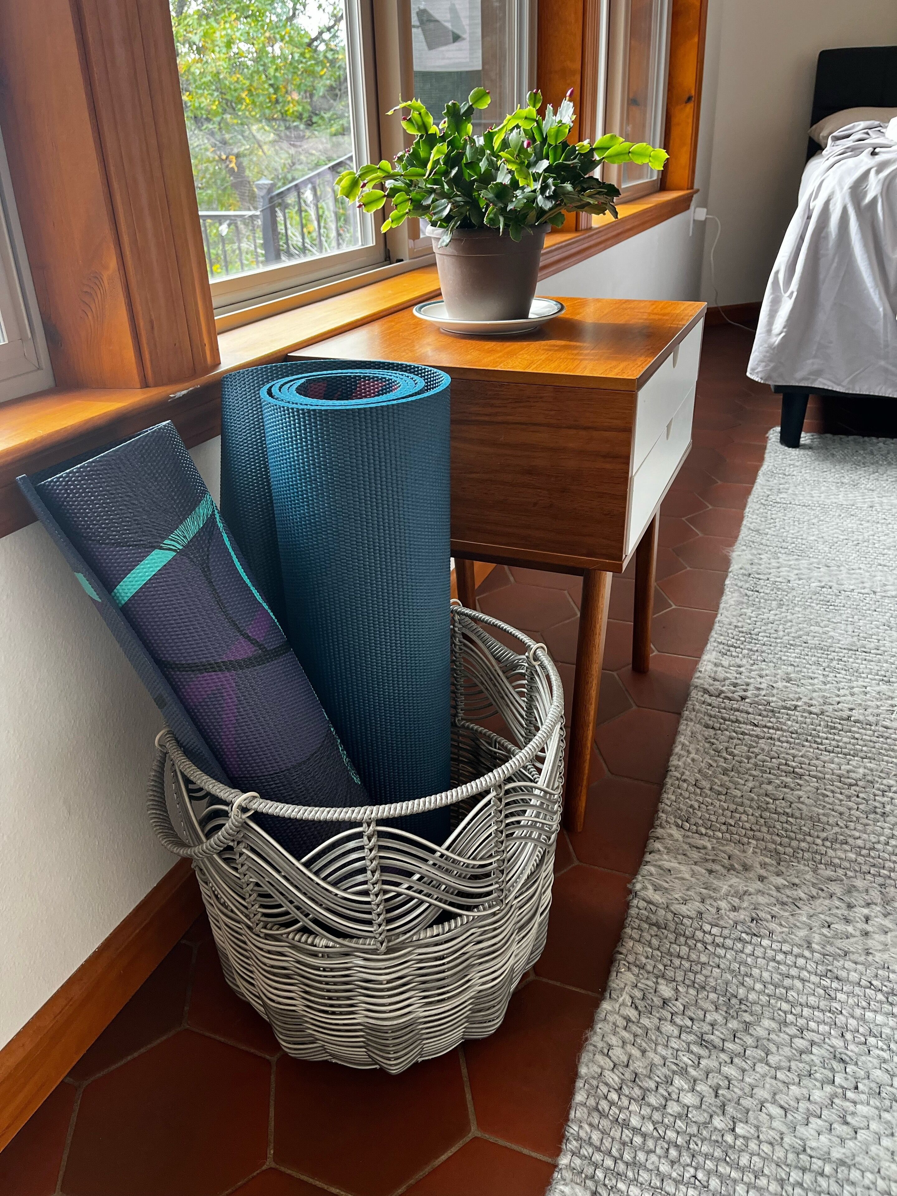 Une pièce avec un bureau en bois, une plante en pot et un panier en osier contenant des tapis de yoga.