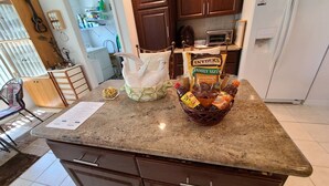 A kitchen with a granite countertop, a basket of snacks, a guitar, and a refrigerator.