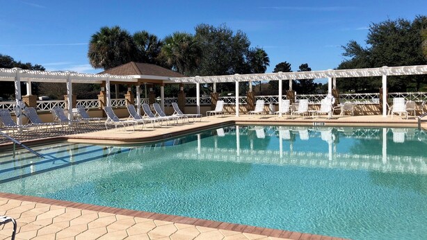A clear swimming pool with lounge chairs and a covered seating area.
