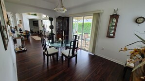 A spacious dining area with a glass table and chairs, a chandelier, and a view through a glass door to an outdoor patio.