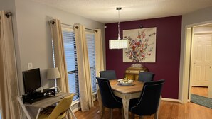 A dining area with a wooden table, four chairs, a television, and a lamp. - Quaint, Quiet, and Comfortable Home Away From Home (Hoover)