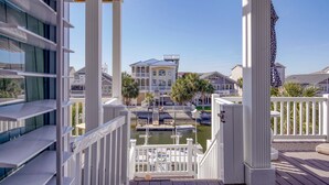 Une vue depuis un balcon donnant sur une marina, avec des bateaux, une grande maison avec un toit bleu et des palmiers.