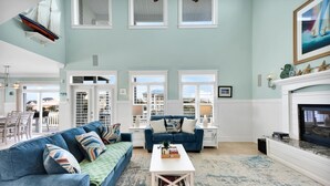 Un salon spacieux avec un plafond haut, de grandes fenêtres, une cheminée et une vue sur l’extérieur.