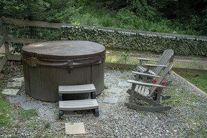 A hot tub, two wooden benches, and a rocking chair in a garden setting with a wooden fence and greenery in the background.