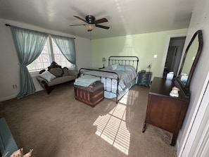 Quarto com cama, penteadeira, mesa de cabeceira, cadeira e ventoinha no teto.