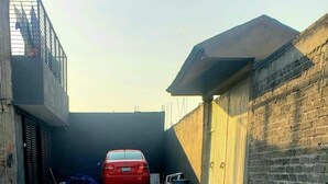 Une cour pavée où est garée une voiture rouge, au centre, et qui est entourée de murs en briques et d’un portail en métal.