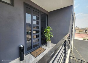 A modern building with a dark facade, a large glass door, a potted plant, and a metal railing. - Beautiful condo with terrace (Los Reyes Acaquilpan)