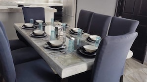 Un espace repas avec une table rectangulaire dressée pour six personnes, entourée de chaises à l’assise rembourrée de couleur bleu foncé.