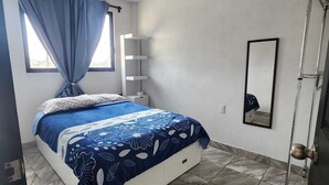 Une chambre à coucher avec un lit, une fenêtre avec des rideaux, un miroir et une porte.