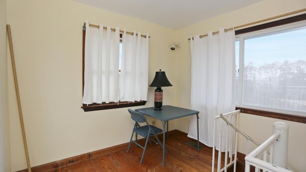 A room with a wooden floor, a table with a chair, a lamp, and a window with curtains. - Oceans of Time (Port St. Joe)