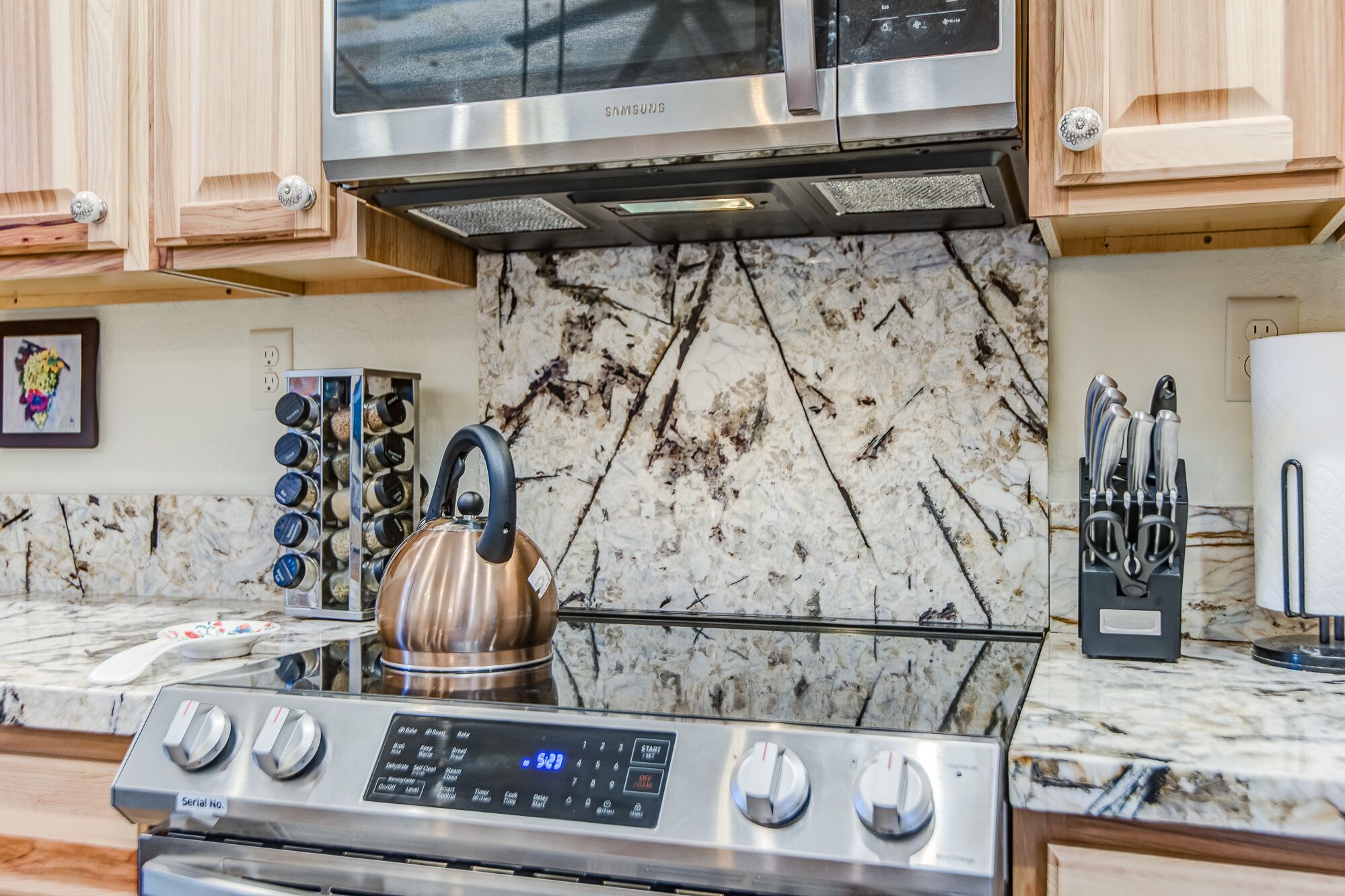 A kitchen with a stainless steel stove, a kettle, and a microwave above it.