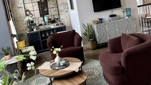 Una sala de estar con pared de ladrillo, un televisor montado en la pared, un ventilador de techo y una zona de comedor con mesa y sillas.