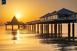 Eine Pier, die sich über ruhiges Wasser erstreckt, mit einem Sonnenuntergang im Hintergrund.