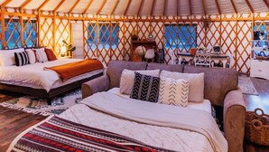 Une yourte avec un plafond arrondi, un lit recouvert d’une couverture à motifs, un canapé et une petite table avec une lampe.