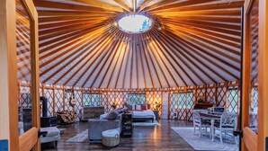 L’intérieur d’une yourte, avec une lucarne circulaire au centre, des poutres en bois et un coin salon accueillant, comprenant un canapé et une table.
