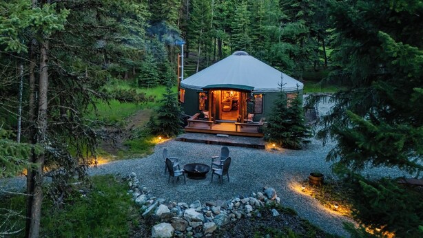 Un chalet confortable avec un toit rond, entouré d’un chemin de gravier et doté d’un espace salon extérieur.