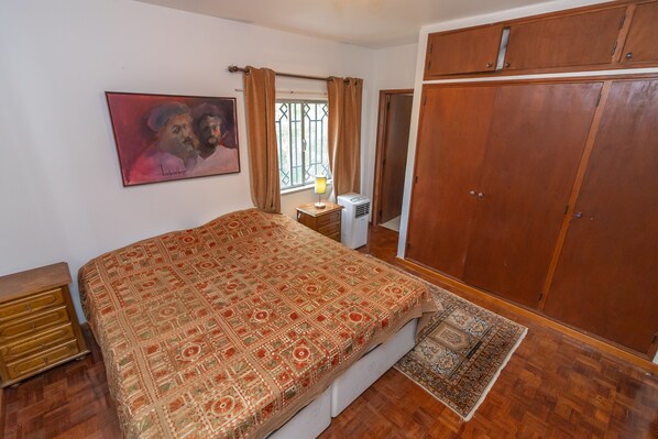 Une chambre à coucher comprenant un lit, une armoire, une table de chevet, une lampe et une fenêtre avec des rideaux.