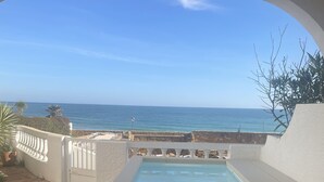 En overdækket terrasse med pool, hvide vægge og havudsigt.