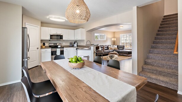 A modern kitchen with white cabinets, a wooden dining table with a bowl of green apples, and a unique woven pendant light. - 🌞 Meridian BNB - 4BR/2.5BA Huge Backyard: Near Eagle, Star, Boise, The Village (Meridian)